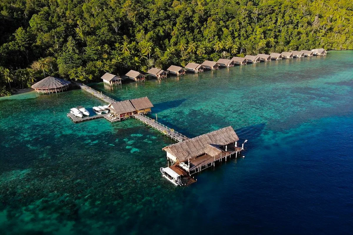 Overwater bungalows along a jungle-covered shore in Raja Ampat