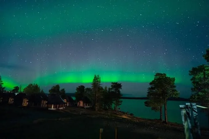 Northern Lights dancing above lakeside cabins in Inari