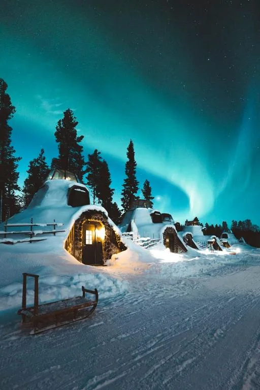 Snow-covered glass igloos glowing beneath the Northern Lights in Rovaniemi