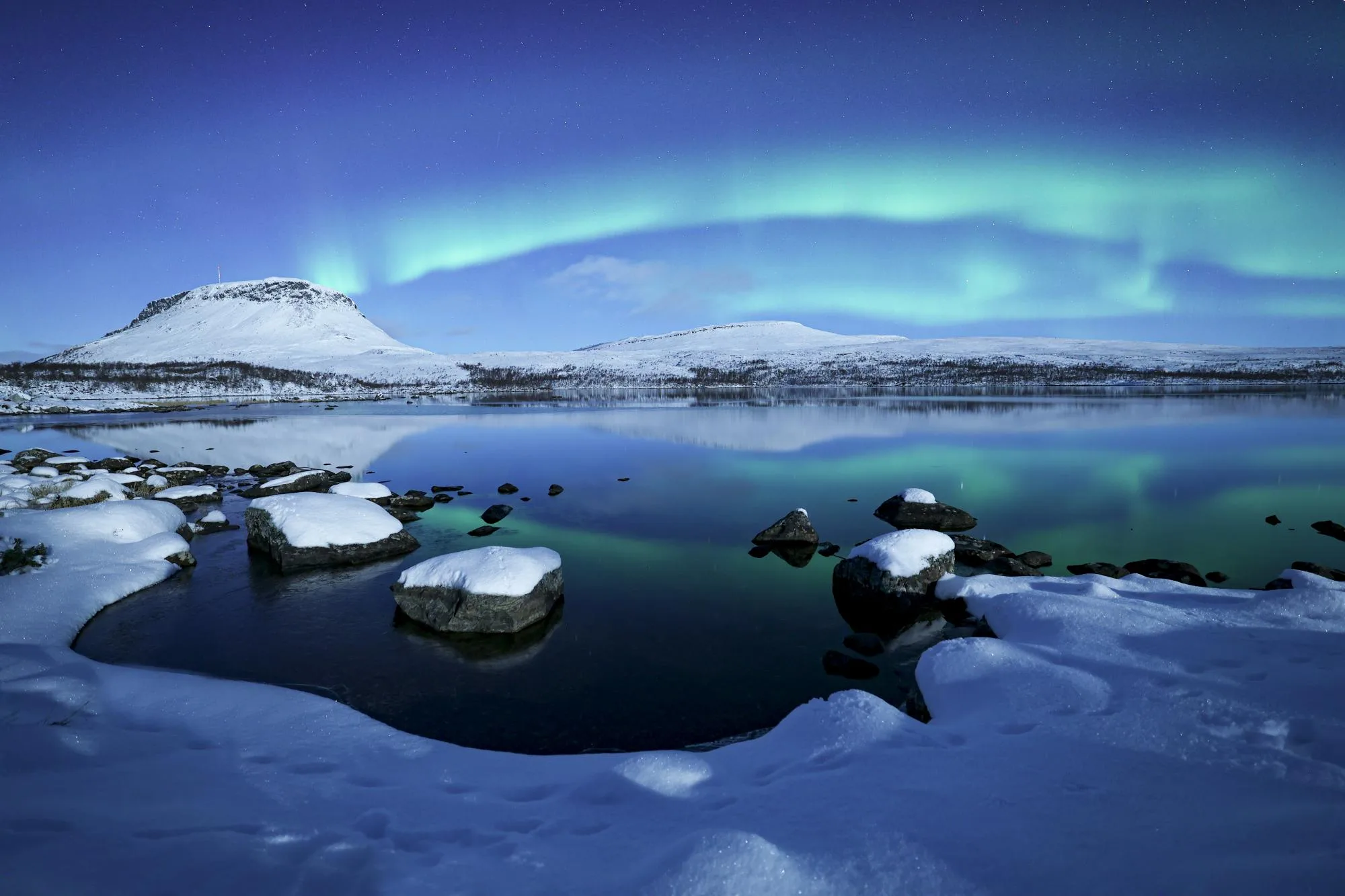 Northern Lights reflected in a still lake below snowy fells in Kilpisjärvi