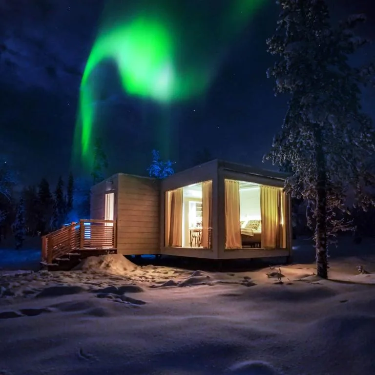 A modern cabin glowing warmly beneath the Northern Lights in Levi