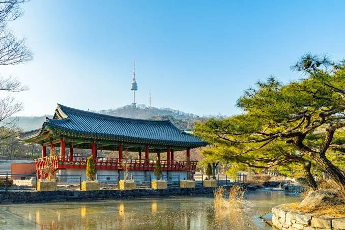 A traditional pavilion beside a pond at Namsangol Hanok Village, with N Seoul Tower behind